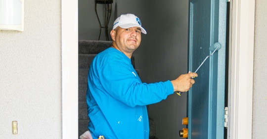 Photo of an ALLBRiGHT PAINTING employee smiling while painting in a door frame.